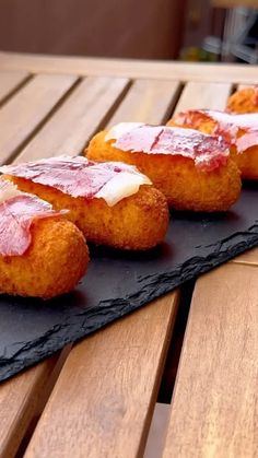 three pieces of food sitting on top of a black slate plate next to a wooden table