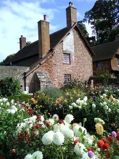 an old brick house surrounded by flowers and greenery