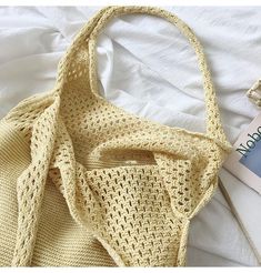 a yellow knitted bag sitting on top of a bed next to a book and magazine