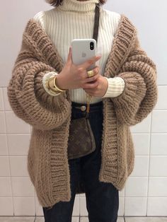 a woman standing in front of a white tile wall holding a cell phone and looking at it