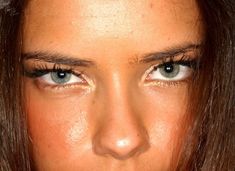 a close up of a woman's face with brown hair and blue eyes looking at the camera