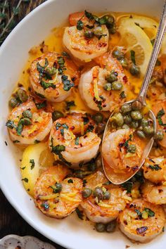 a white bowl filled with cooked shrimp and capers on top of a wooden table