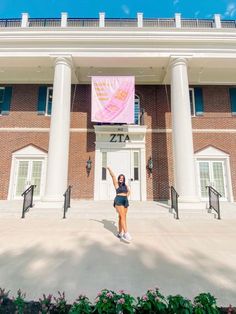 a woman standing in front of a building with her arms up and one hand raised