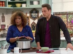 a man and woman standing in front of a pot on a kitchen counter with pots