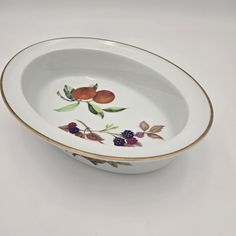 a white bowl with fruit painted on the side and gold trimming around the rim