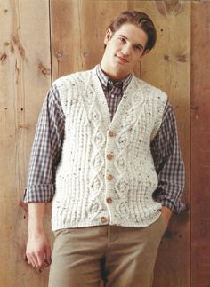 a man standing in front of a wooden wall wearing a white vest and plaid shirt