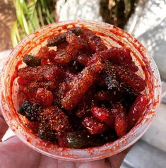 a hand holding a bowl full of food with red sauce on the top and meat in the middle