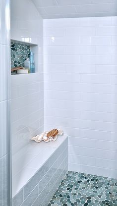 a white tiled bathroom with blue and green tiles on the shower wall, along with an open shelf