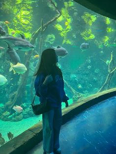 a woman standing in front of an aquarium looking at fish