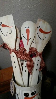 some wooden spoons with snowmen painted on them are in a pail and tied to a wall