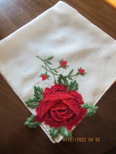 a red rose on a white napkin sitting on a wooden table next to a knife