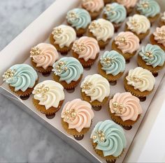 an open box filled with cupcakes on top of a marble countertop covered in frosting