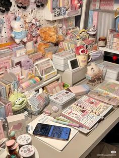 a desk with many items on it and a phone in the foreground that is full of stuff