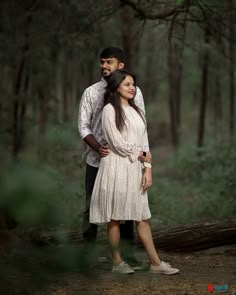 a man and woman standing next to each other in the woods