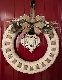 a christmas wreath hanging on a red door with the words joy to the world in it