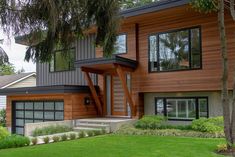 a modern house with wood siding and green grass in the front yard, along with trees