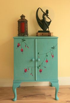 a blue cabinet with red flowers painted on it and a clock sitting on top of it