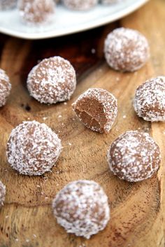 some powdered sugar balls are on a wooden table next to a plate with chocolate