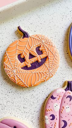 three decorated cookies sitting on top of a white tray next to purple and blue plates