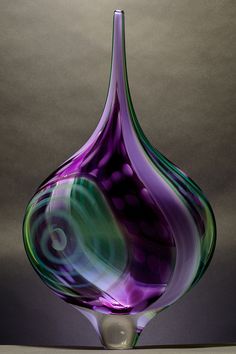 a purple and green glass vase sitting on top of a wooden table next to a gray wall