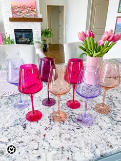 four wine glasses sitting on top of a counter next to a vase filled with tulips