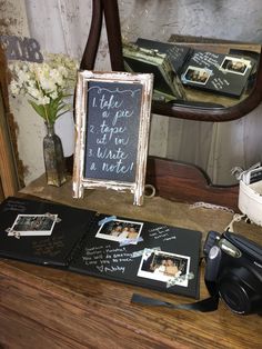 a wooden table topped with pictures and a chalkboard sign next to a pair of camera's