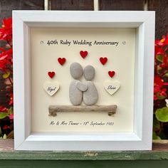 a white frame with two rocks and hearts in the shape of a couple sitting on a log