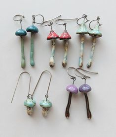 six different colored earrings are displayed on a white surface, with one dangling from the ear