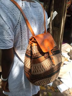 a woman carrying a brown and tan woven purse on her back with an orange strap