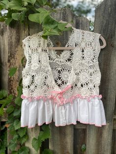 a white top with pink trims hanging on a wooden fence next to green leaves