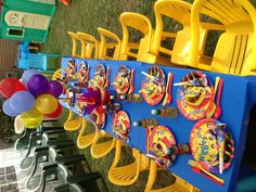 a blue table topped with yellow plastic chairs and plates covered in colorful paper napkins