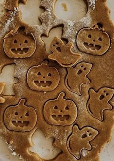 some cookies shaped like pumpkins and ghost faces are on a plate with powdered sugar