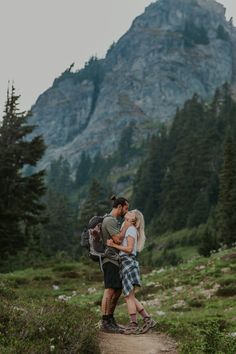 a man and woman hugging each other while standing on a trail in front of a mountain