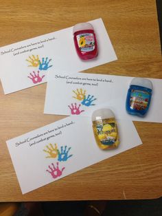 three handprinted cards on top of a wooden table with two bottles of glue