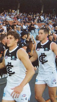 two male afl players are walking in front of an audience