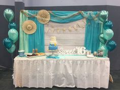 a table topped with a blue cake and lots of balloons in front of a curtain