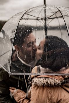 two people are kissing under an umbrella in the rain while another person is standing behind them