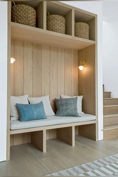 a wooden bench with two pillows on it in front of some stairs and baskets hanging from the wall