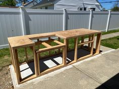 three wooden tables sitting on top of a sidewalk next to a white fence and grass