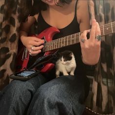 a woman playing guitar with a cat sitting on her lap next to her and looking at the camera