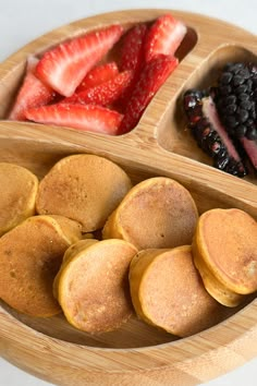 a wooden plate topped with pancakes, berries and strawberries next to another plate filled with fruit