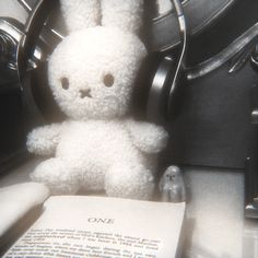 a white stuffed animal sitting on top of a table next to an open book and headphones