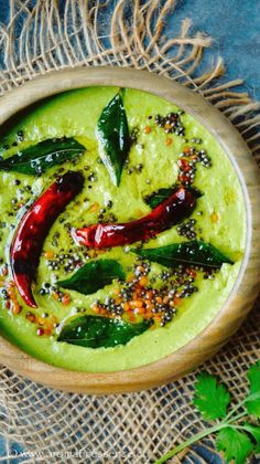 a wooden bowl filled with guacamole and topped with red peppers, green leaves and seasoning