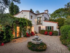 a white house with a fountain in front of it and lots of greenery on the outside