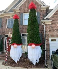 two tall trees with red bows on their heads are in front of a brick house