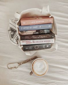 a stack of books sitting on top of a bed next to a cup of coffee