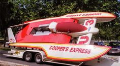 a red and white boat is on the back of a trailer with trees in the background