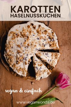 a cake with white frosting sitting on top of a wooden table next to a flower