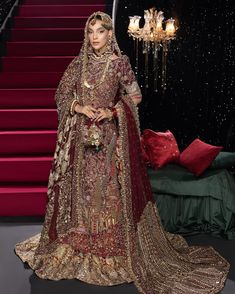 a woman in a red and gold bridal gown standing next to stairs with chandelier