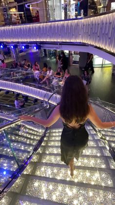 a woman is walking down the stairs in a shopping mall with lots of lights on them